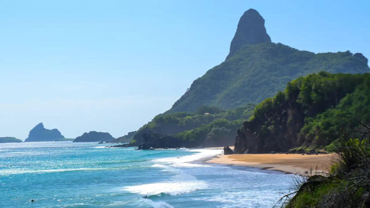 praia com água azul e montanha de fernando de noronha ao fundo