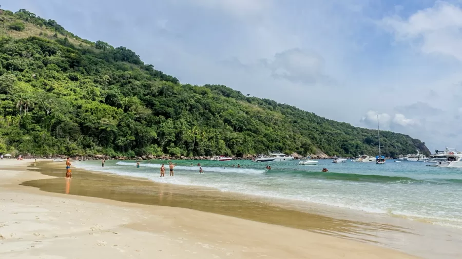 orla da praia com pessoas entrando no mar e paisagem verde ao fundo