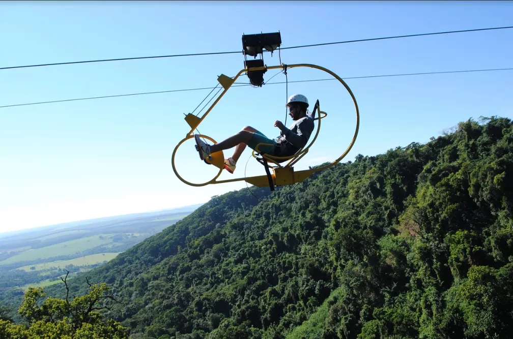 homem pedalando em tirolesa com vista de montanhas ao fundo