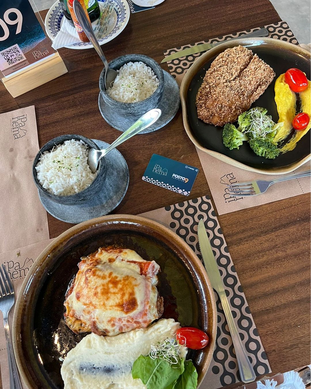 mesa posta em restaurante de BH com dois pratos servidos com carne e purê, acompanhados de duas porções pequena de arroz.